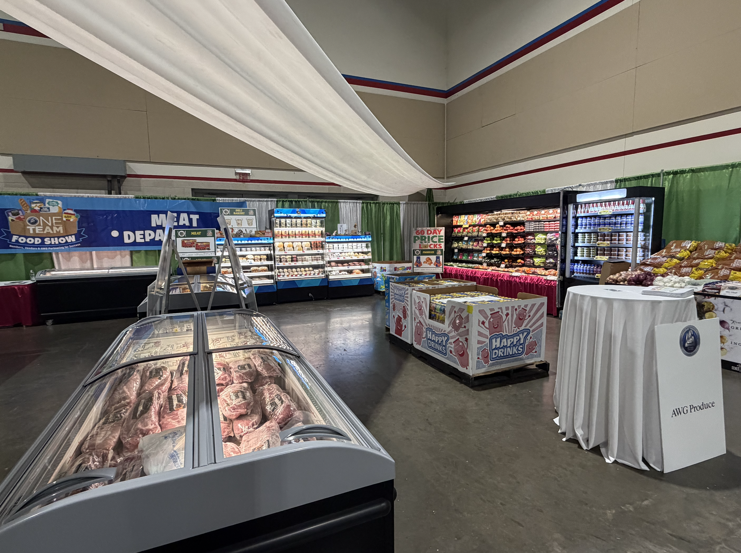 An indoor grocery store display with various fresh produce, meats in a freezer, and packaged goods, with signs advertising prices and products.