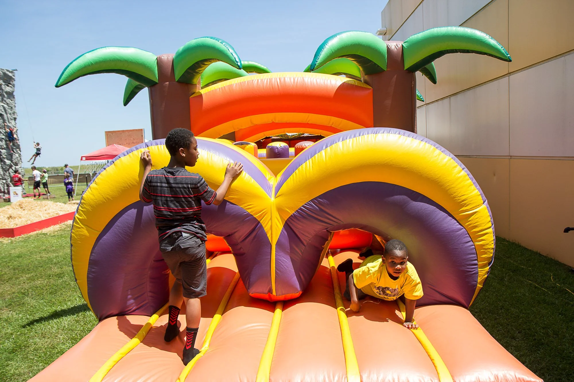 Two children playing on a colorful inflatable jungle-themed bounce house outdoors on a sunny day.