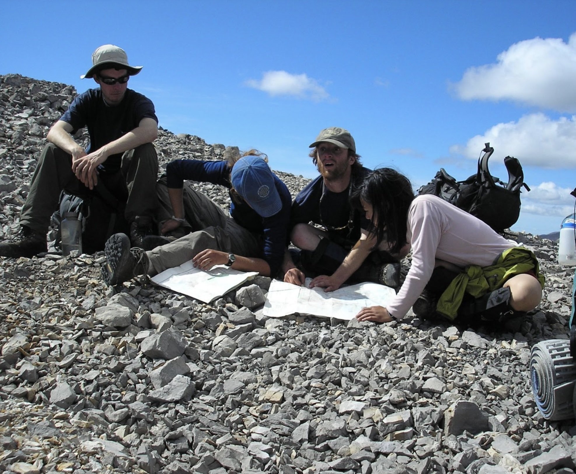 Close-up of a hand with an orange sleeve gently touching purple and white wildflowers in a natural outdoor setting.