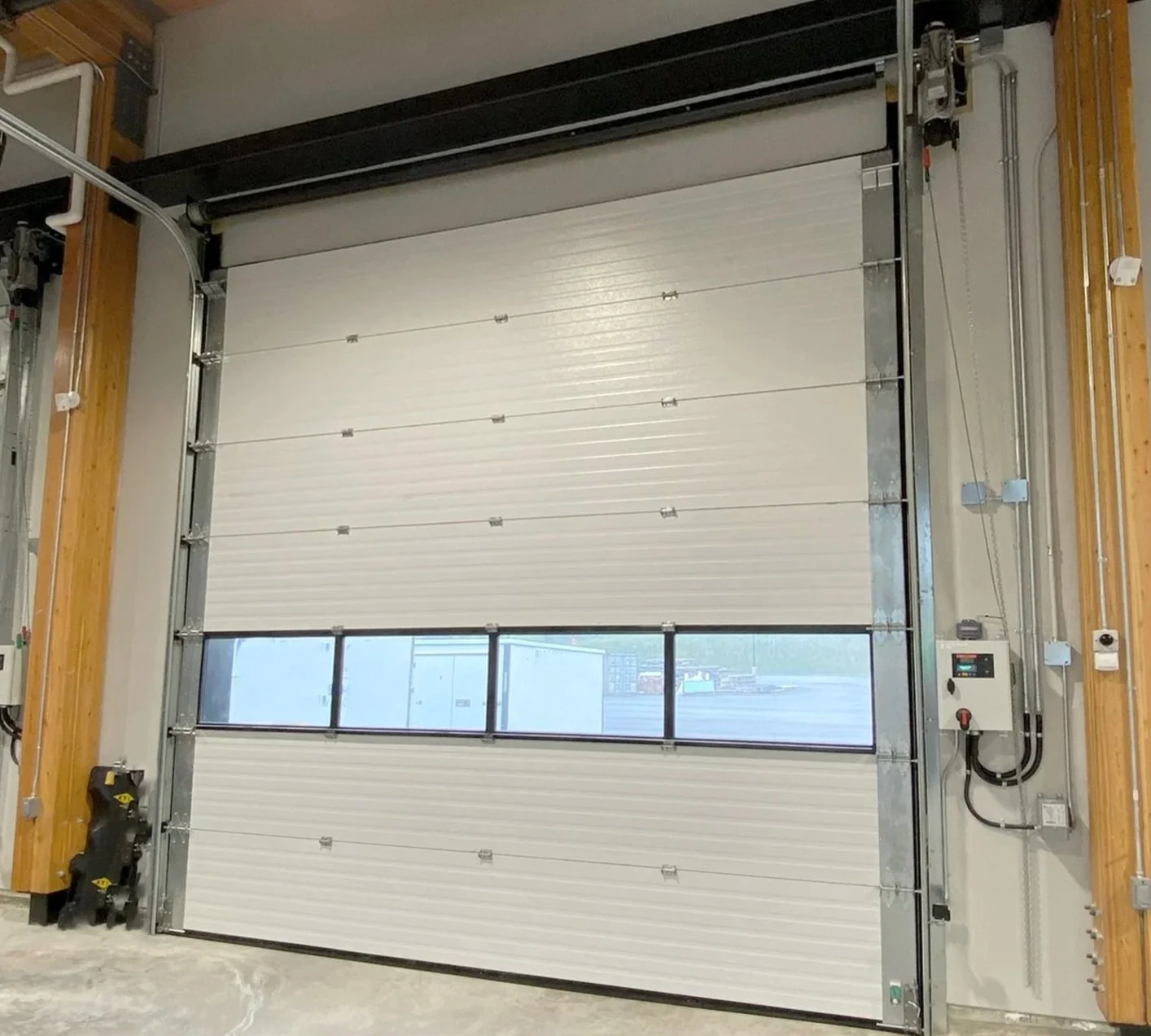 Automated rolling garage door with a window panel at the bottom, partially open, in an industrial setting.