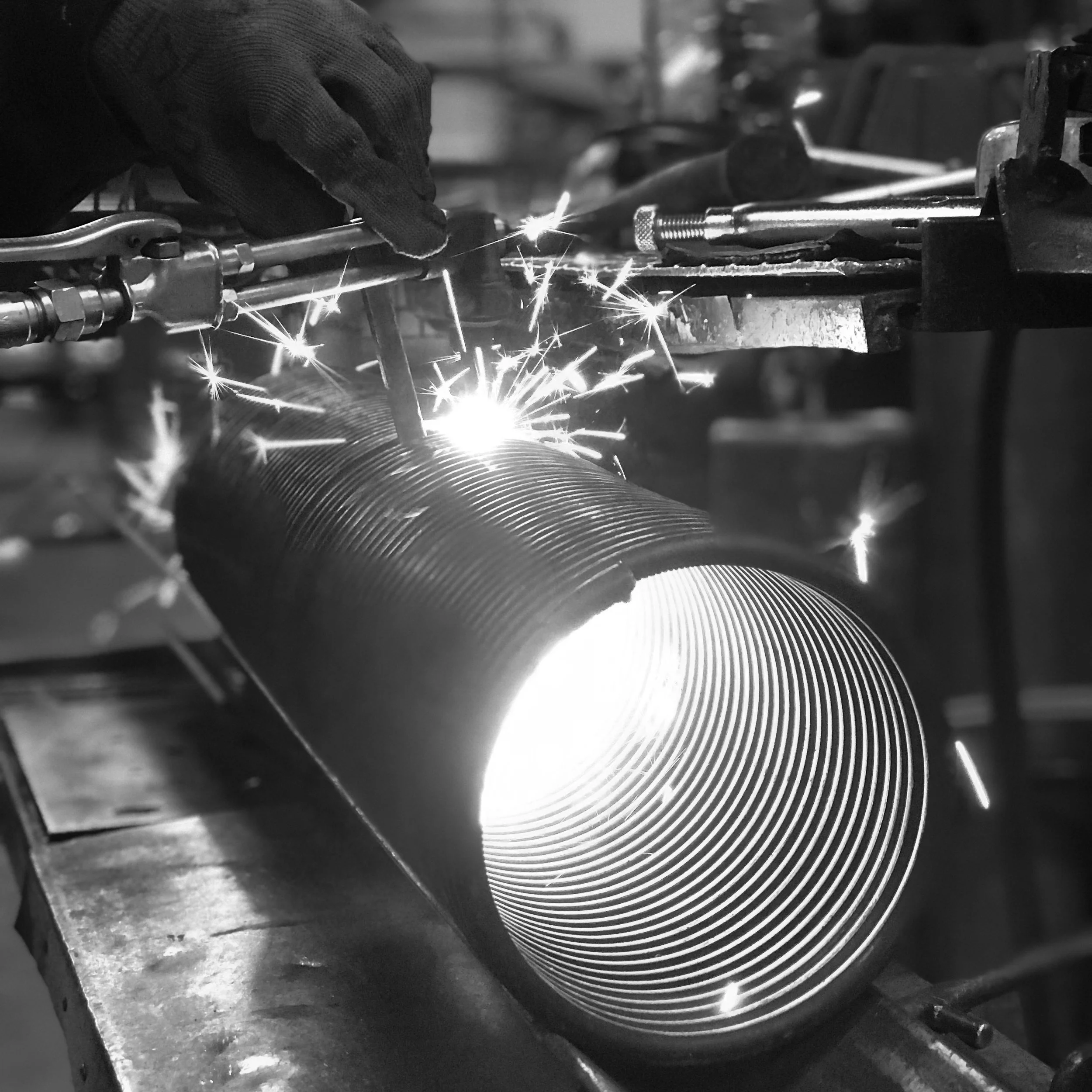 A worker wearing gloves is welding a metal pipe, producing sparks in a workshop.