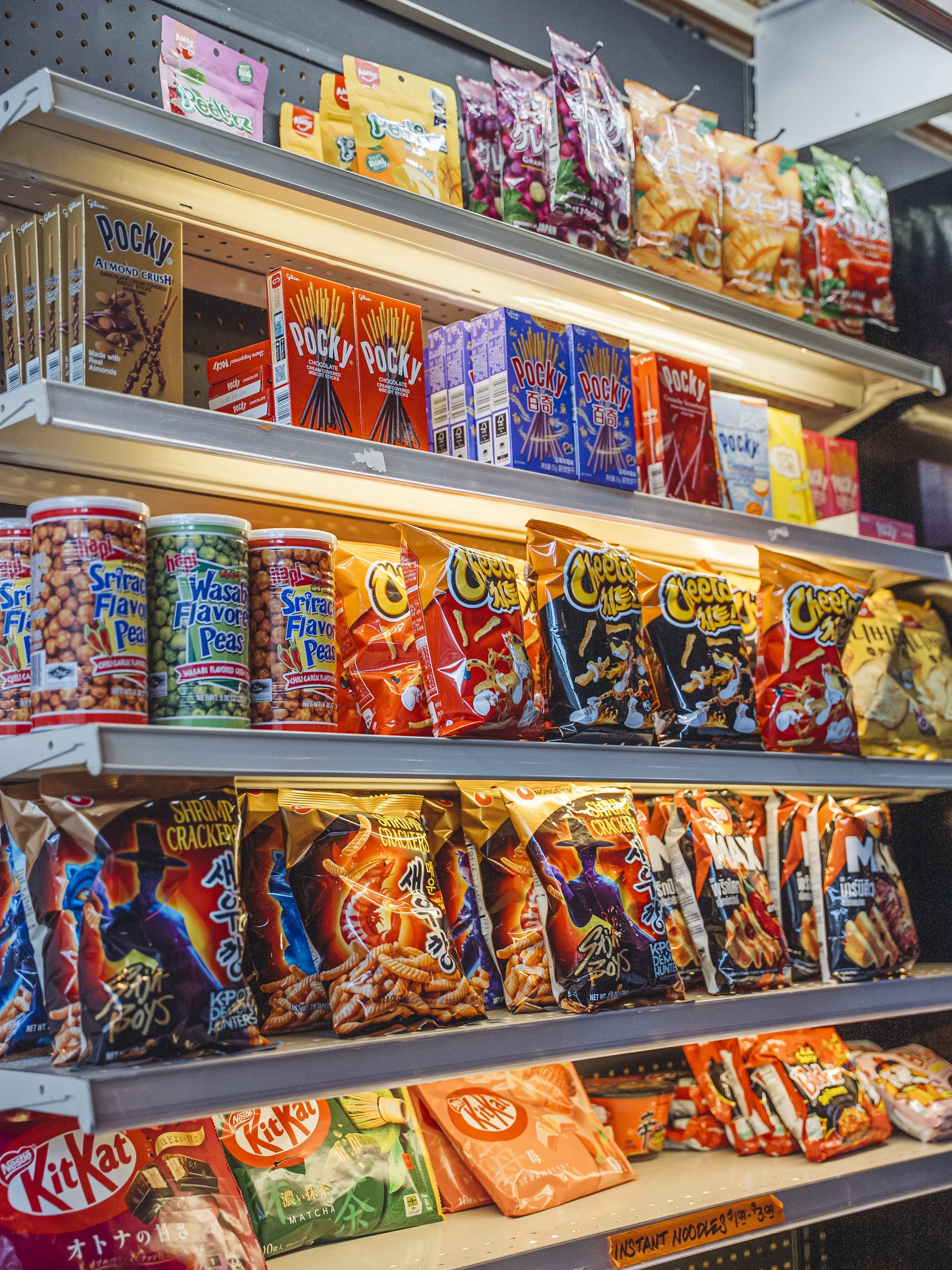 Store shelves stocked with various snack foods including Pocky, snack crackers, wasabi peas, and assorted packaged snacks.