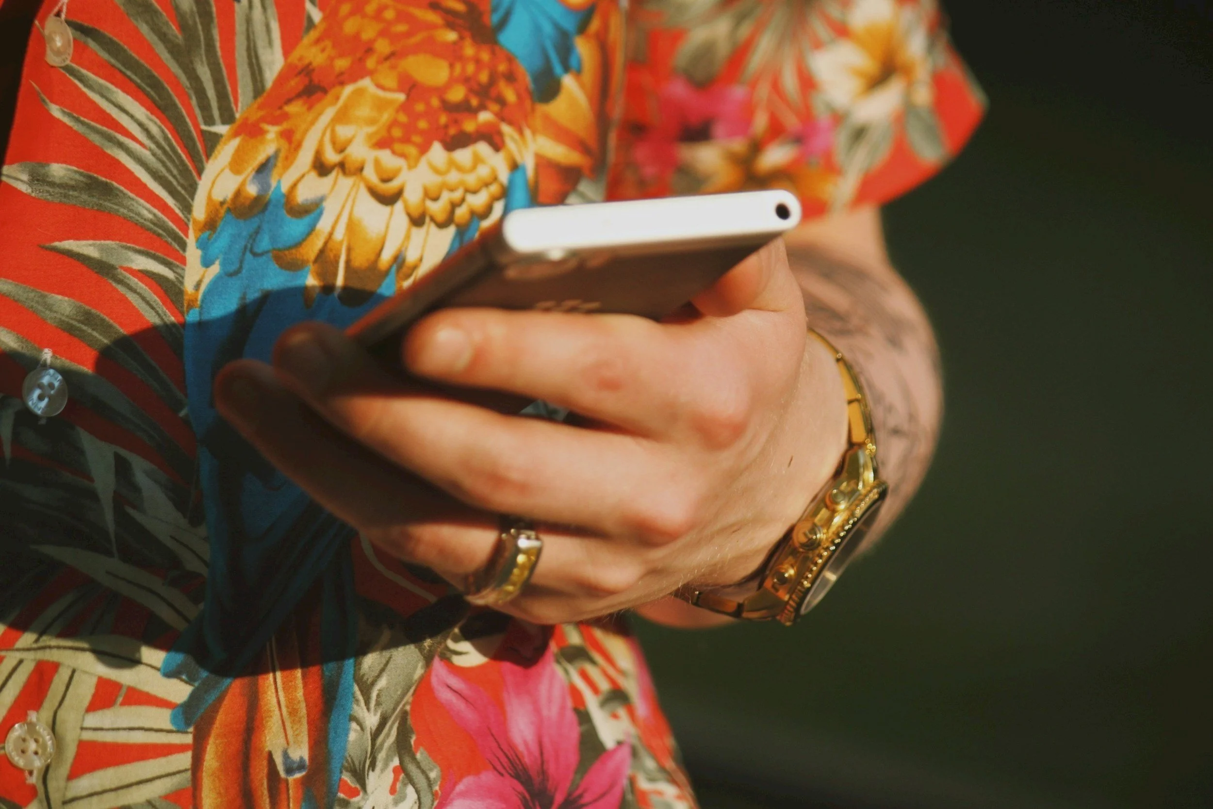 Person holding a smartphone with a tropical floral shirt and jewelry