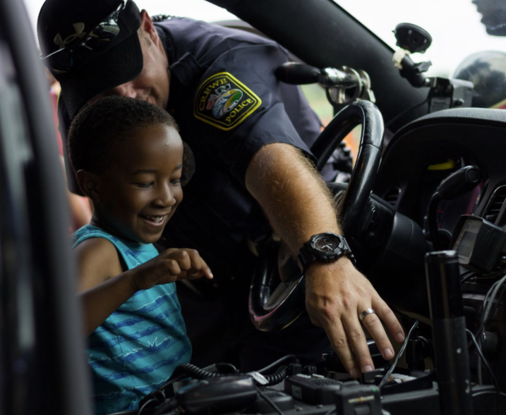 A police officer demonstrating the equipment inside a police vehicle to a young boy who looks excited and happy.