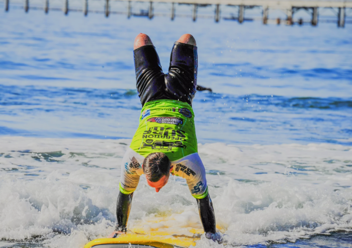 Surfer performing a handstand on a surfboard in the water near a pier.