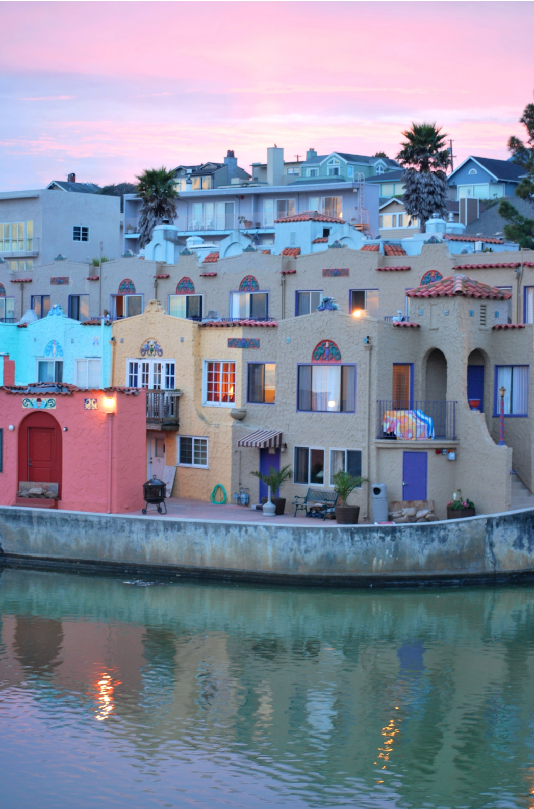 Colorful Mediterranean-style houses on a canal at sunset with pink and purple sky.
