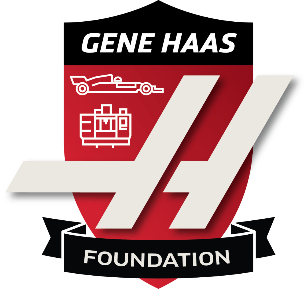 A logo for the Gene Haas Foundation featuring a red shield with white and black accents. It includes icons of a race car and a CNC machine, with stylized white 'GH' initials, and the words 'Gene Haas Foundation'.