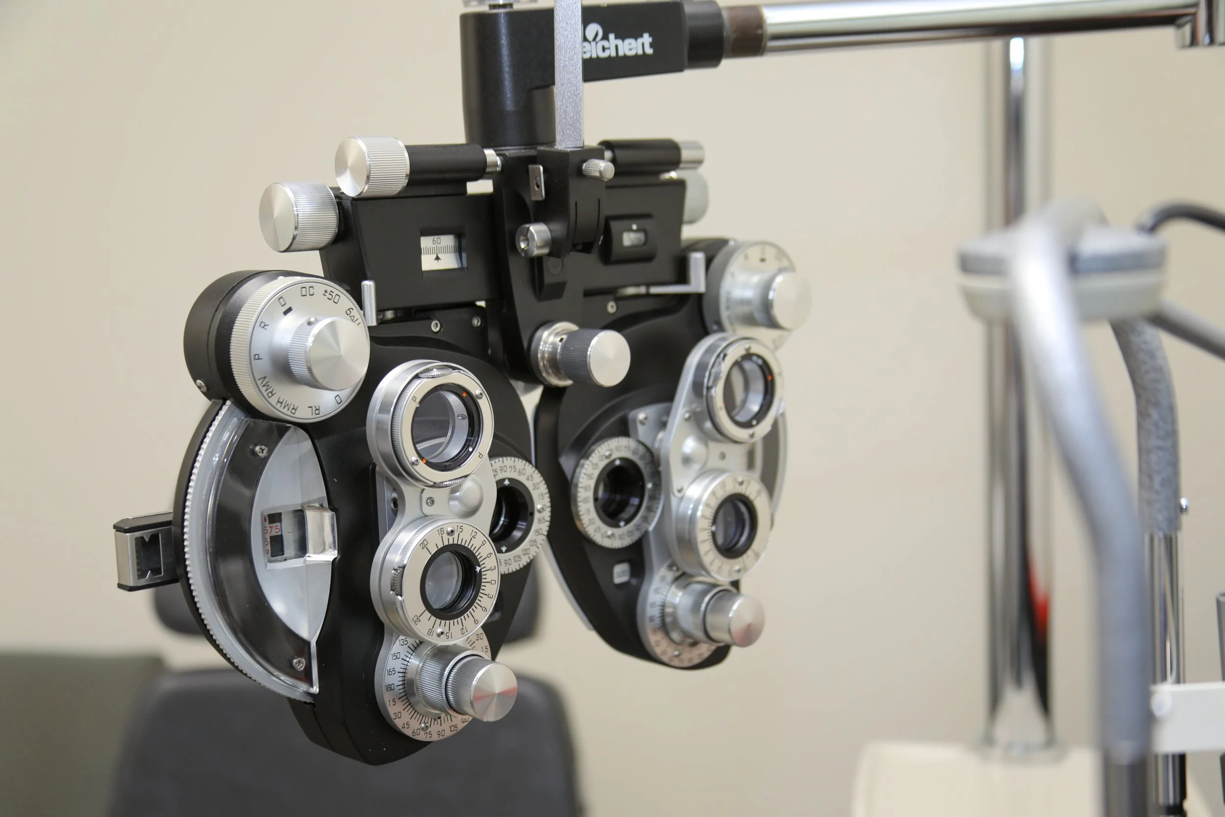 Close-up of an ophthalmic trial lens rack with multiple adjustable metallic lenses, dials, and knobs, used for eye examinations.