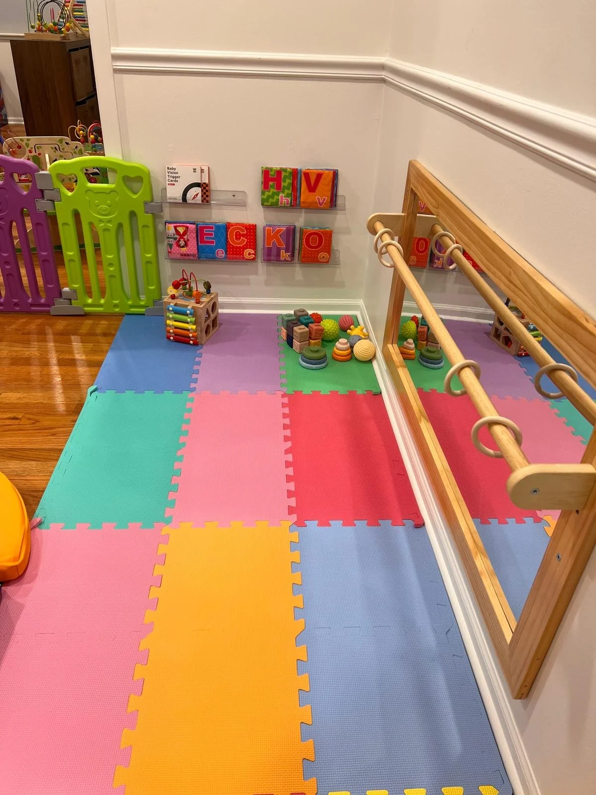 Children's play area with colorful foam mats, wooden climbing bars, and toy blocks and balls.