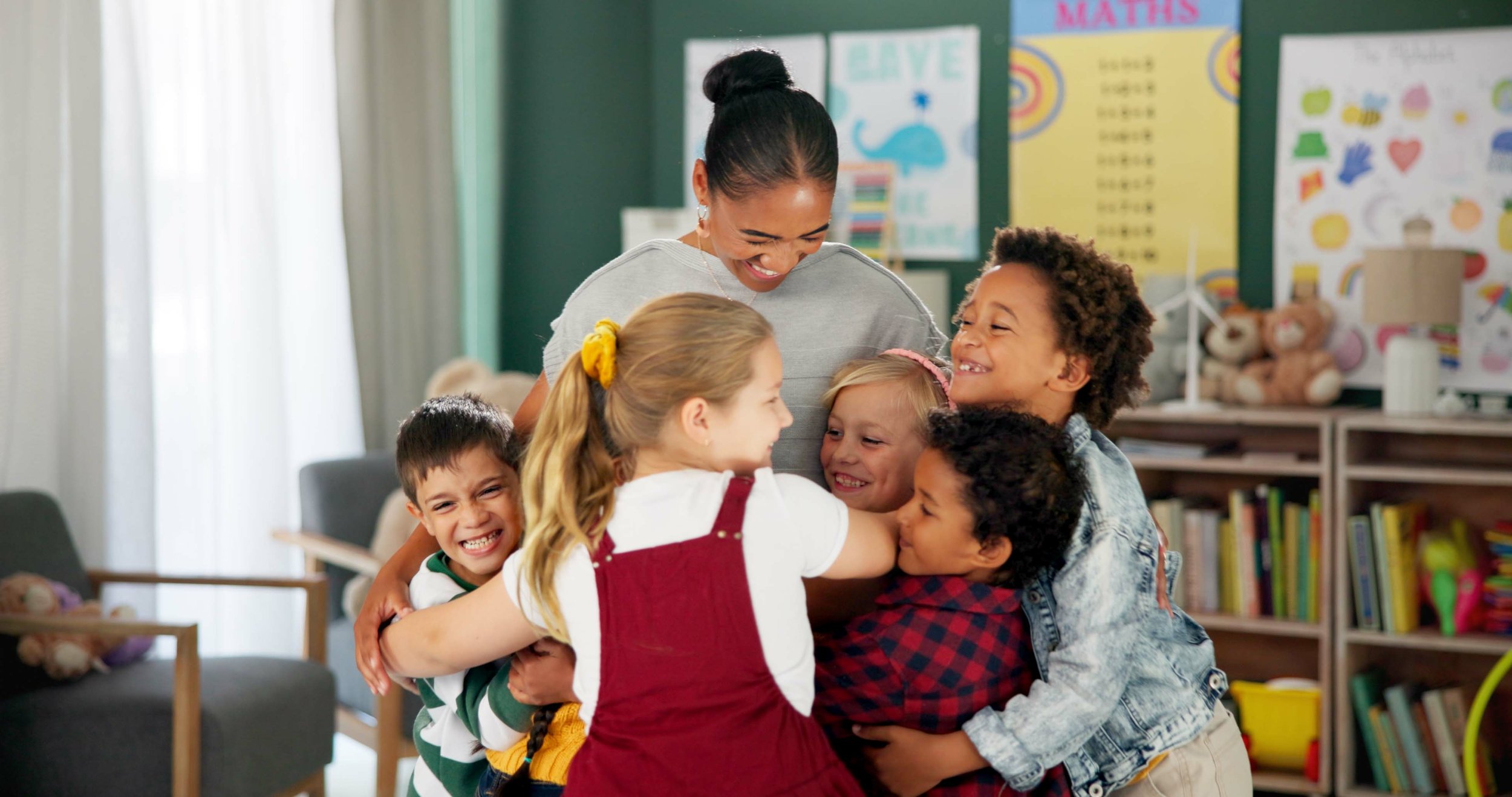 Group of children and a woman hugging and smiling in a classroom.