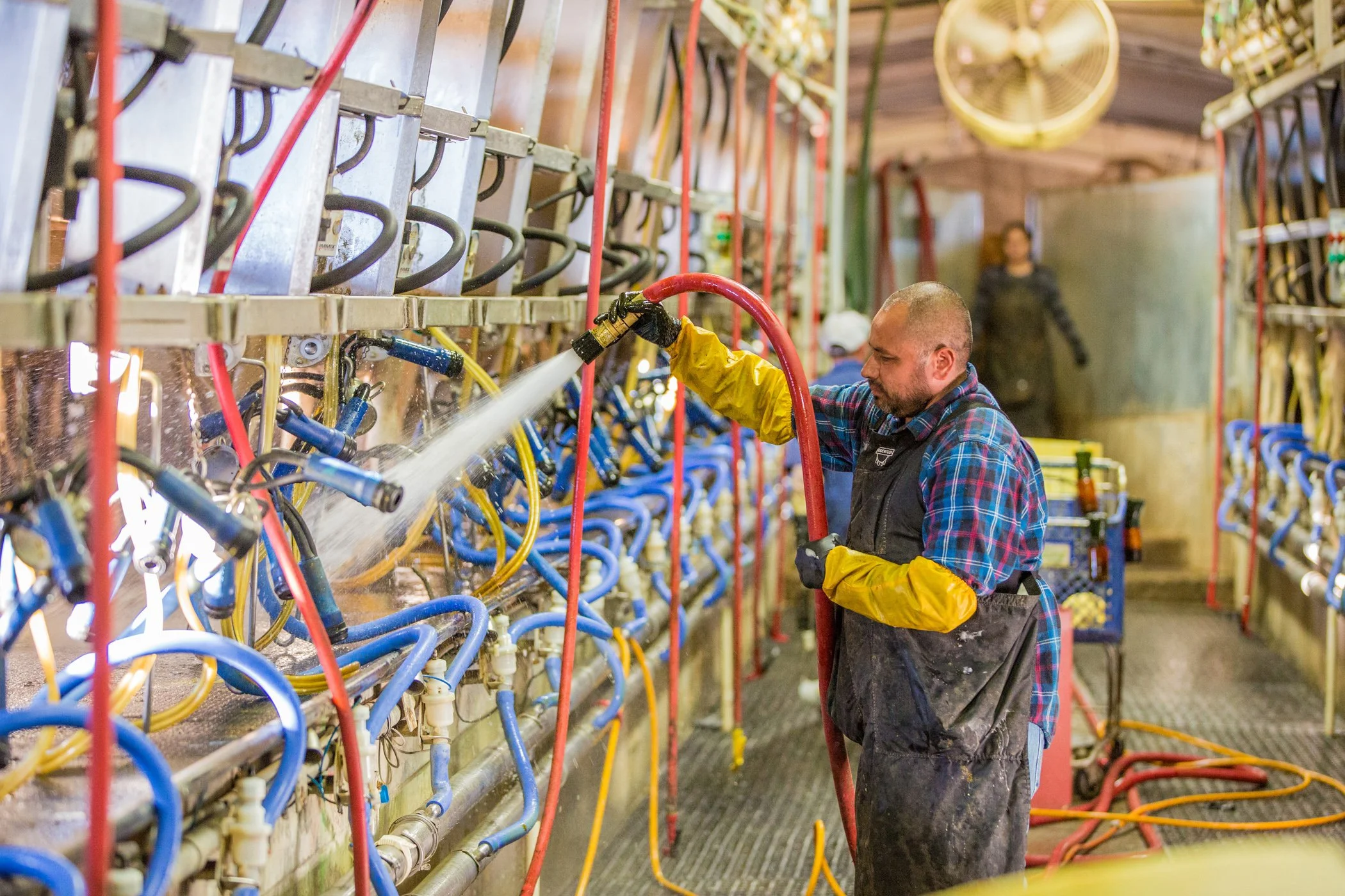 A man washing a large machine with multiple hoses and pipes in a workshop.