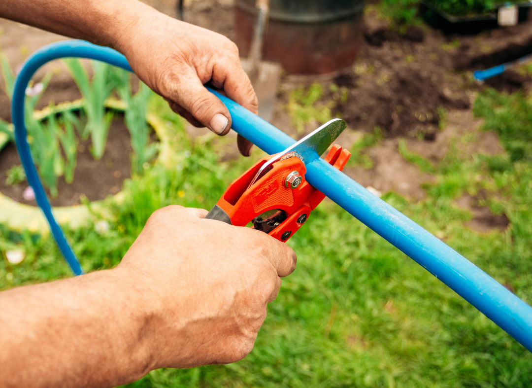 A person cutting a blue water pipe with a pipe cutter tool outdoors