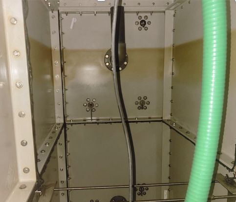 Inside a metal enclosure with multiple screw holes and a black cable hanging from the top center. A green corrugated tube is on the right side.