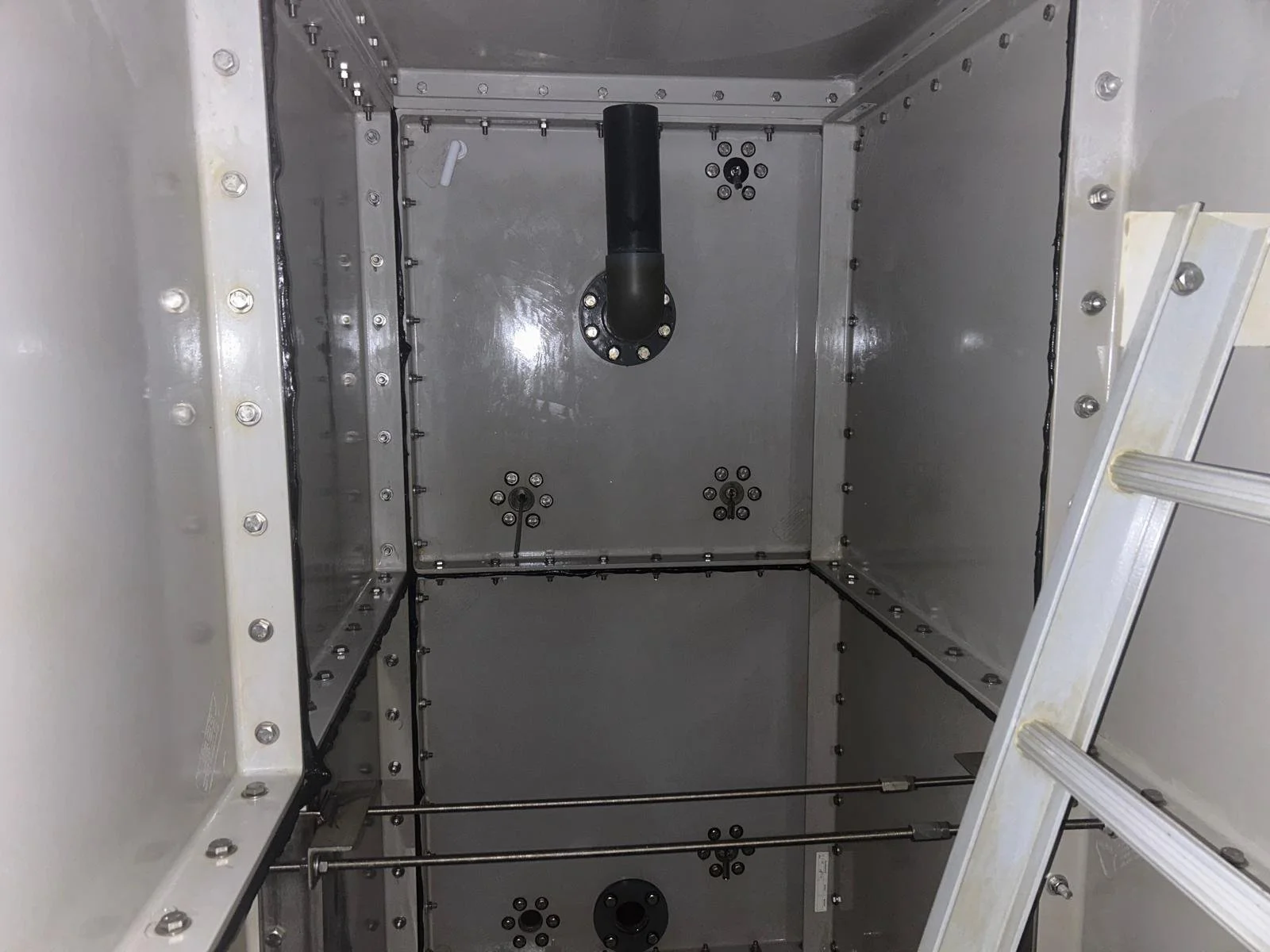 Interior of an industrial or scientific metal enclosure with bolted panels, some rods, and a ladder on the right side.