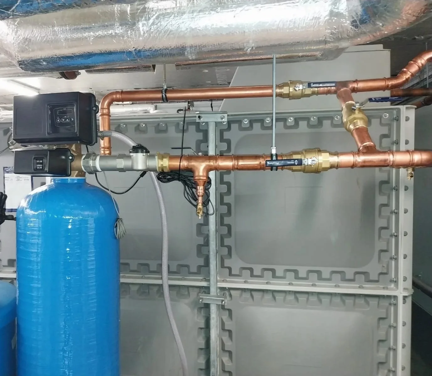 Industrial water treatment system with copper and brass piping, a large blue tank, and control valves.