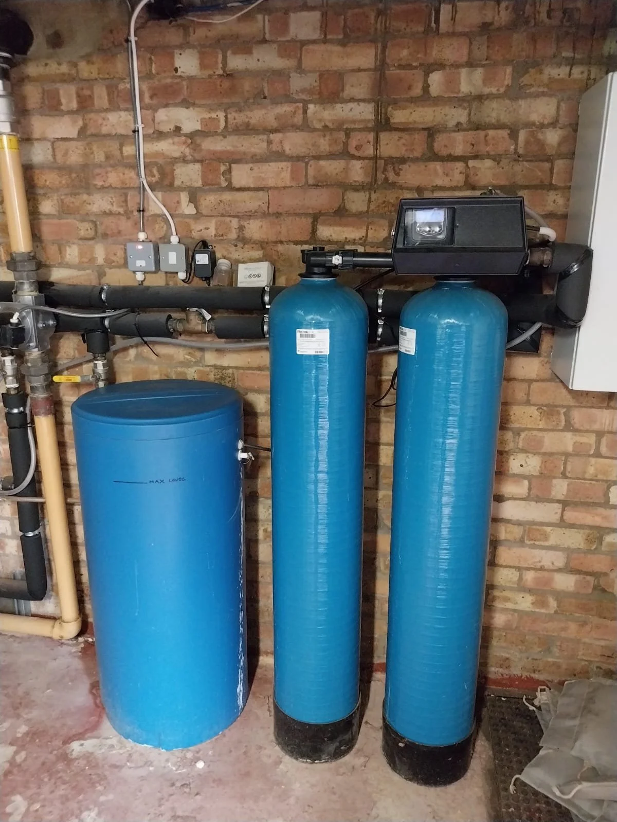Water treatment system with three large blue tanks connected to black pipes against a brick wall.