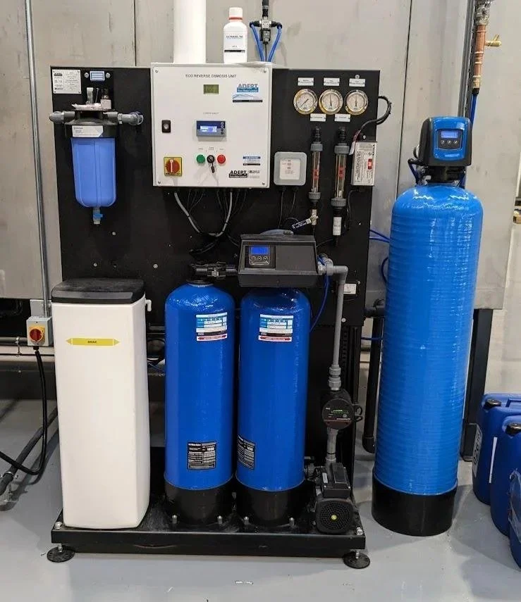 Water treatment system with blue filters, gauges, control panel, and various pipes and components in an industrial setting.
