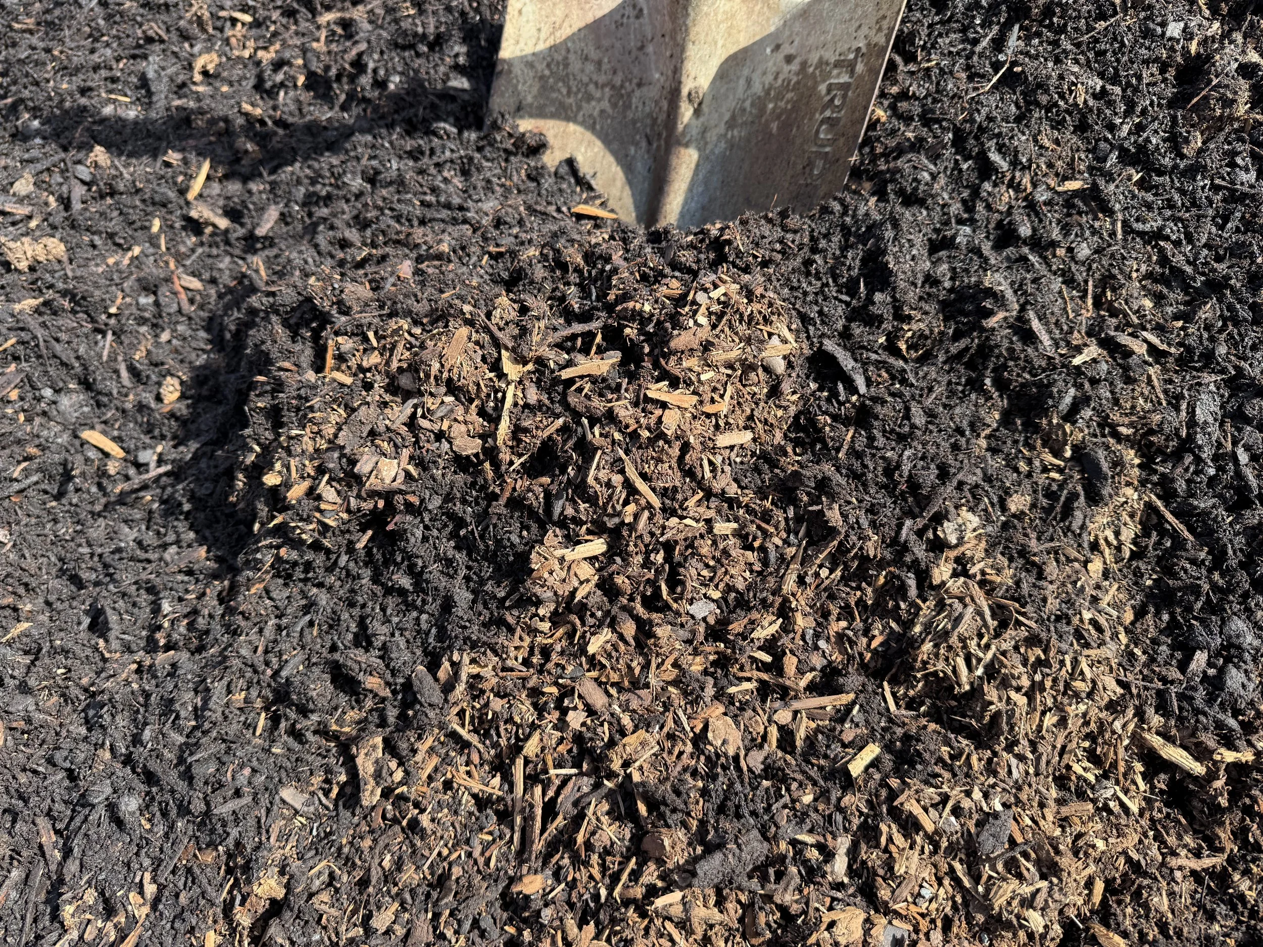Multiple piles of different colored gravel and soil with concrete blocks in an outdoor yard, trees and a blue sky in the background.