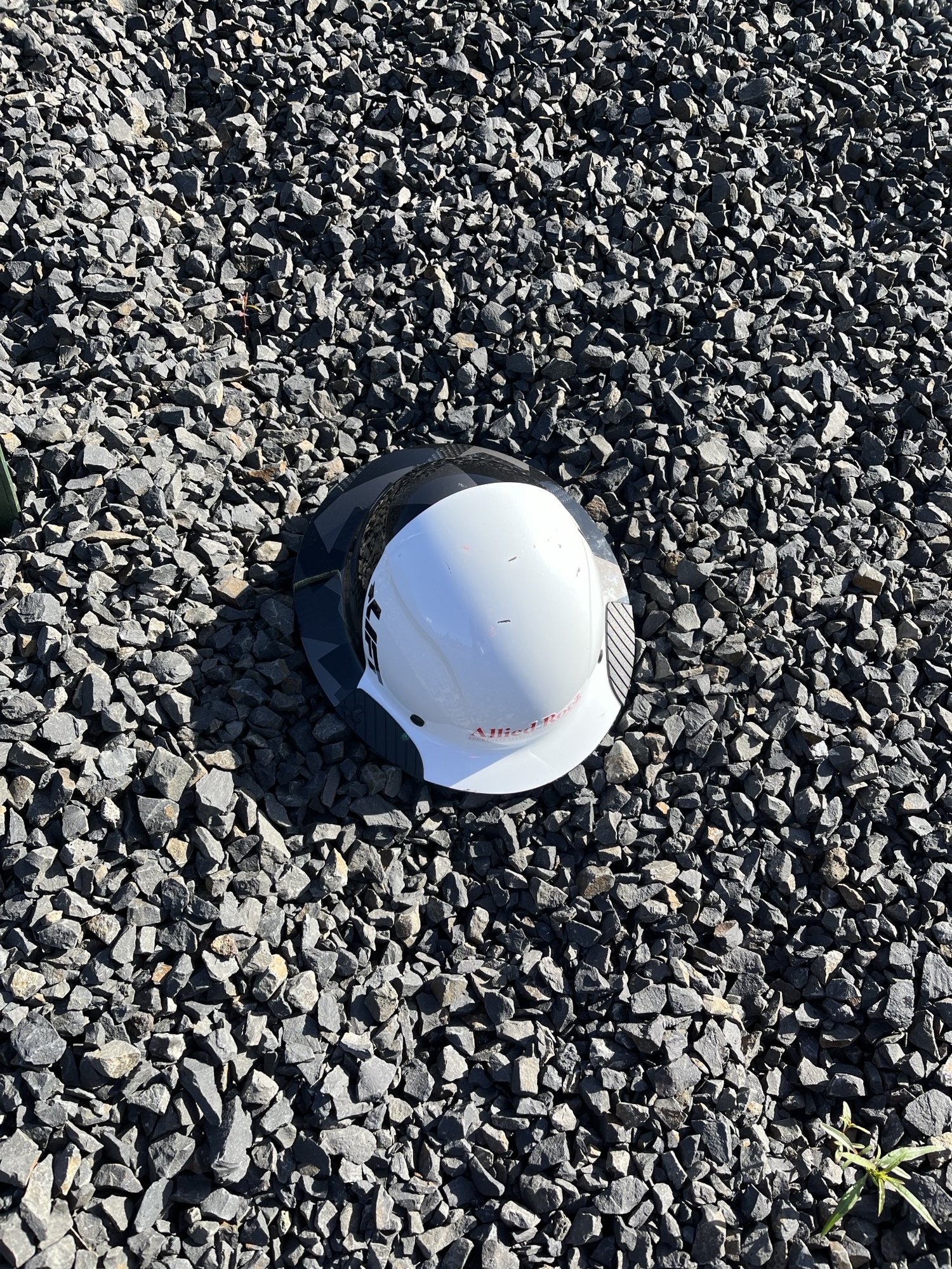 A white construction hard hat lying on a bed of gray gravel stones.