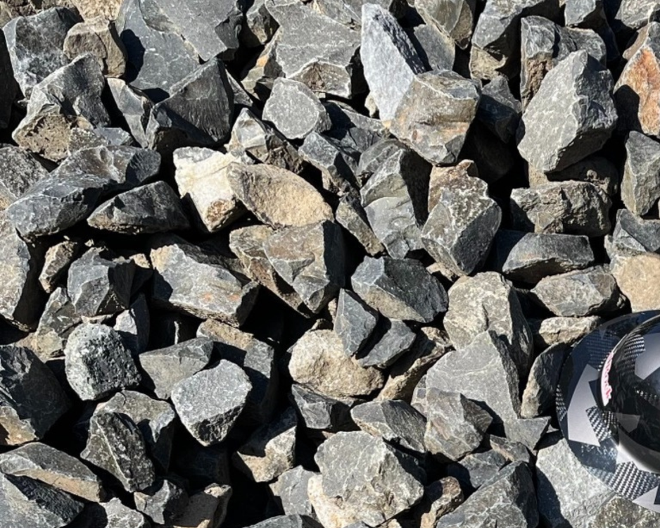 A pile of gray and black irregularly shaped rocks with a small black and white rock with a pattern in the lower right corner.