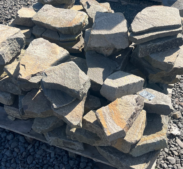 Pile of irregularly shaped natural gray rocks stacked on a wooden pallet outdoors.