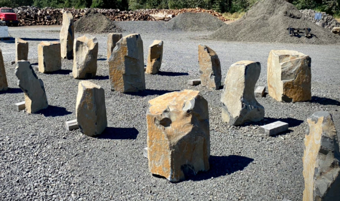A lineup of large, rough cut stones placed on gravel at an outdoor site.