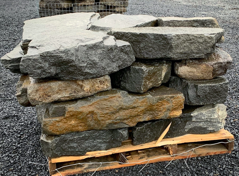 Stack of large gray and brown rocks on a wooden pallet, set on gravel surface.