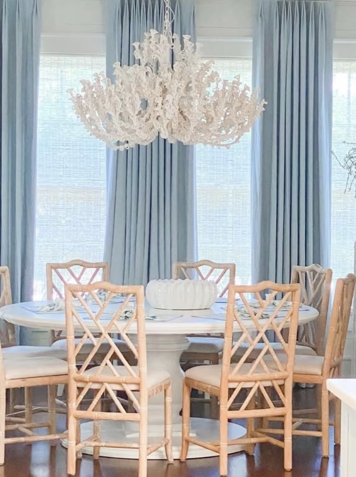 Dining room with a round white table, eight wooden chairs, blue curtains, and a large white chandelier.