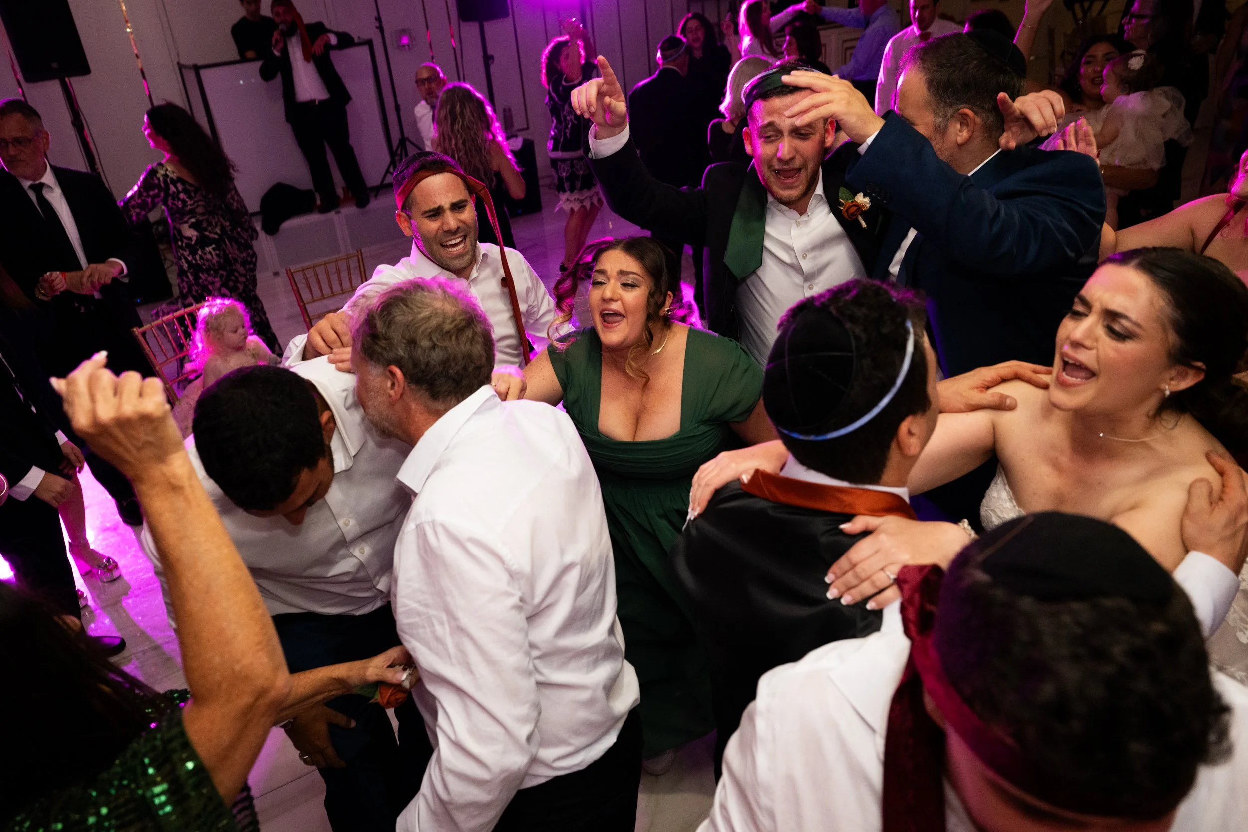 People dancing and celebrating at a wedding reception with joyful expressions and lively movements.