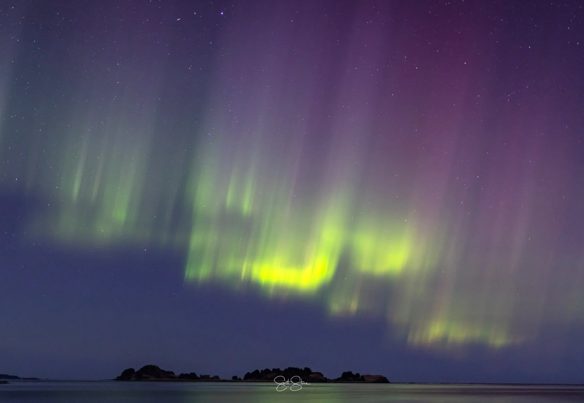 Northern lights (aurora borealis) illuminating the night sky above a body of water and distant islands.