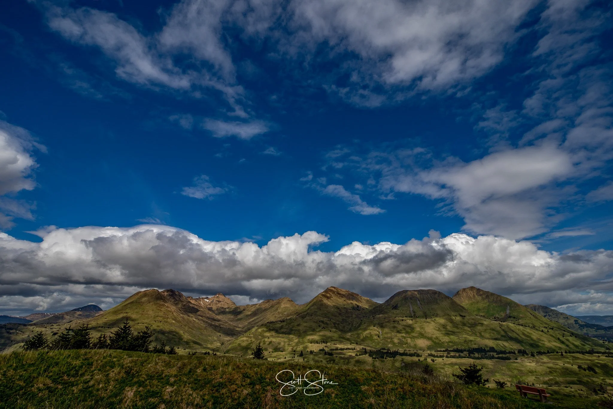 Scenic view of green rolling hills and mountains under a partly cloudy blue sky.