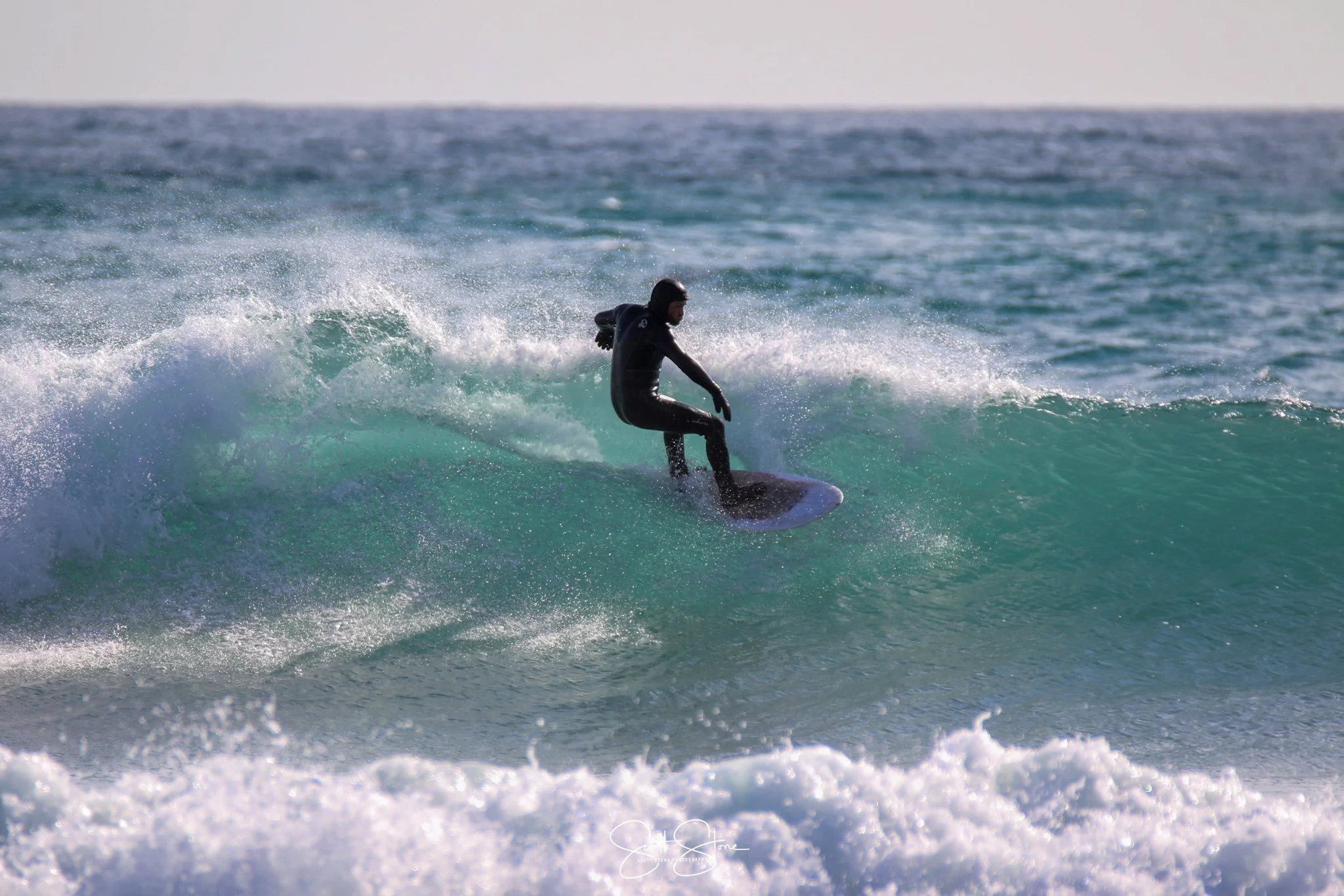 A person wearing a black wetsuit surfing on a blue wave in the ocean.