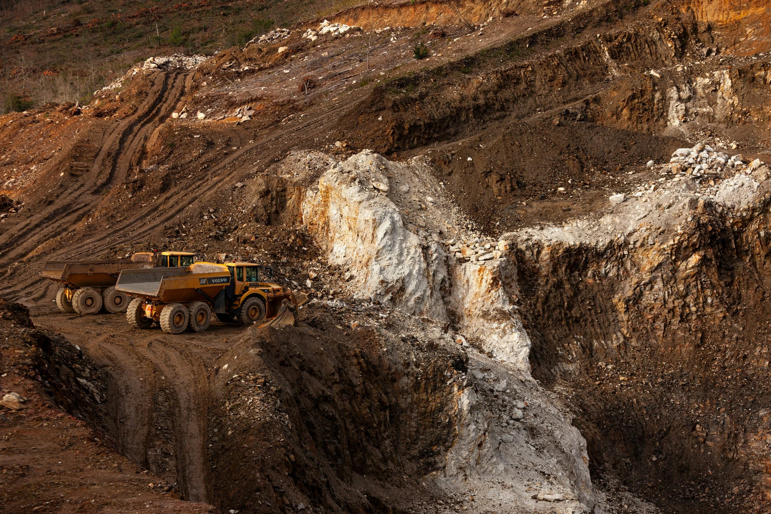 Two large yellow construction vehicles working on dirt and rock at a quarry or excavation site with visible layers of earth.