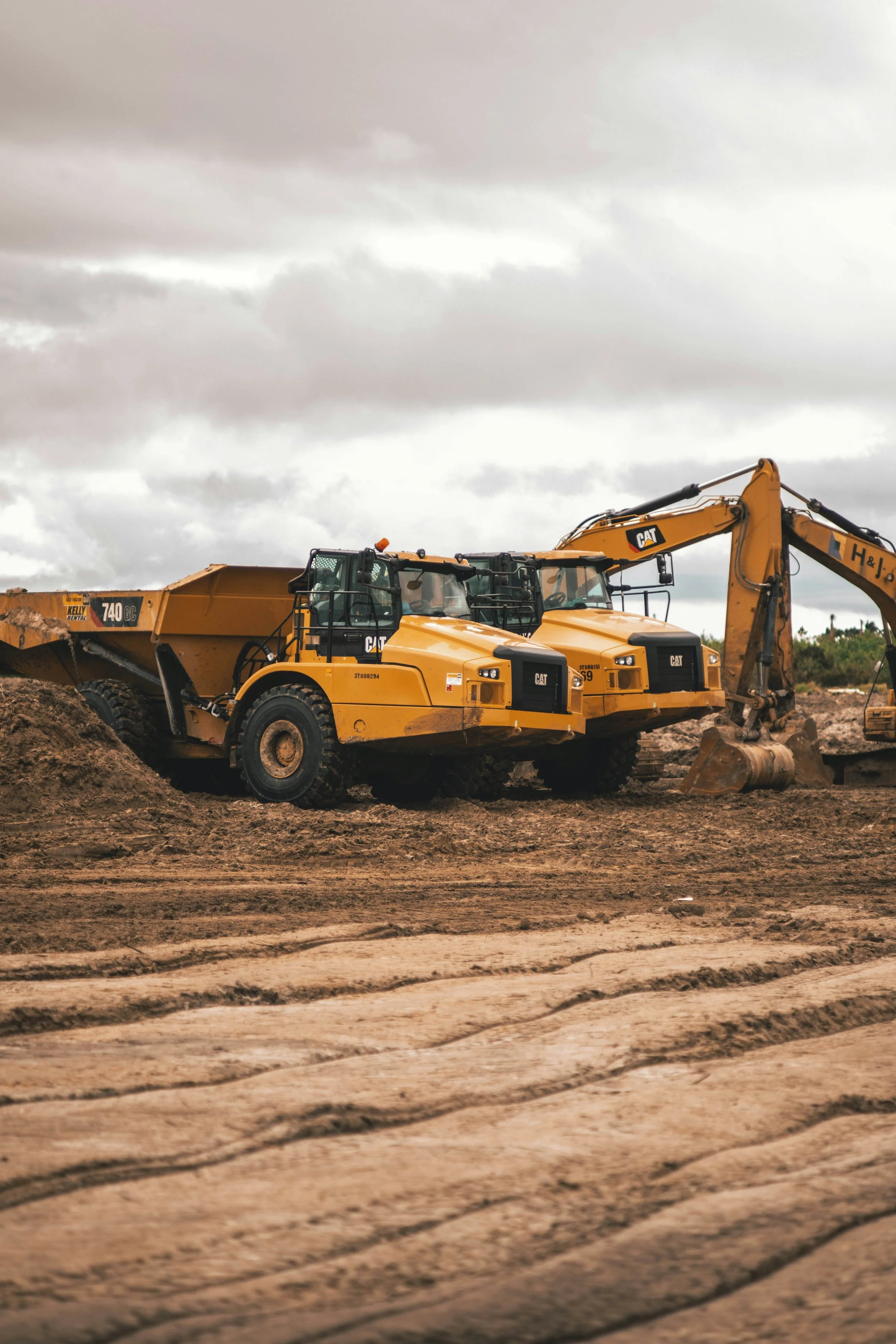 Two large Caterpillar construction vehicles in a dirt field with cloudy sky overhead.