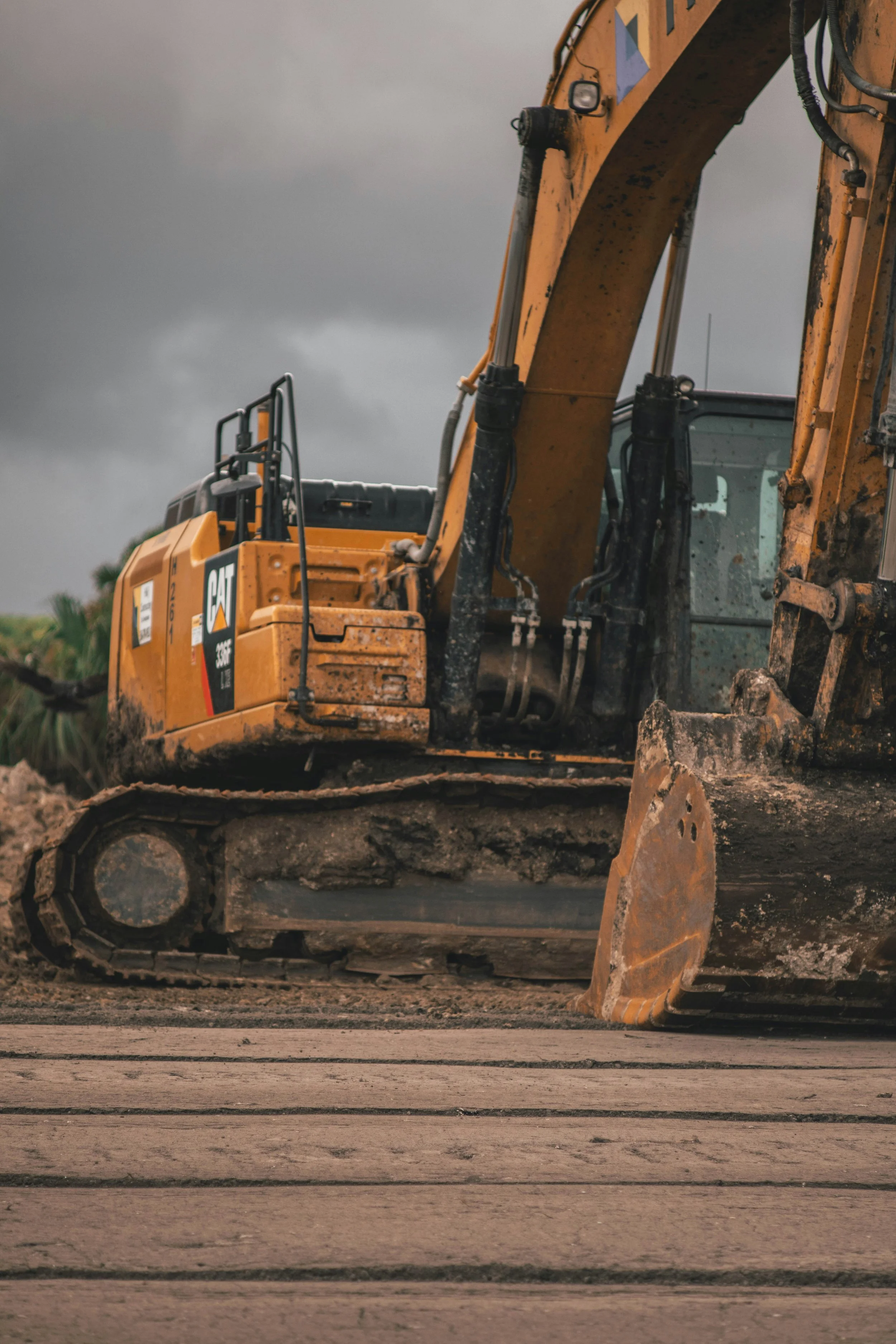 A yellow Caterpillar excavator working on a construction site with dark cloudy skies overhead.