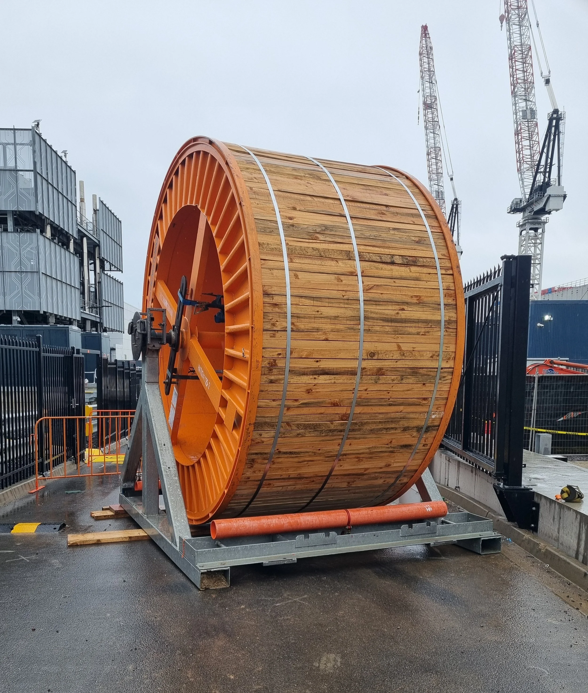 A large electrical cable drum sits in an A-Frame cable stand on a driveway in a data centre.