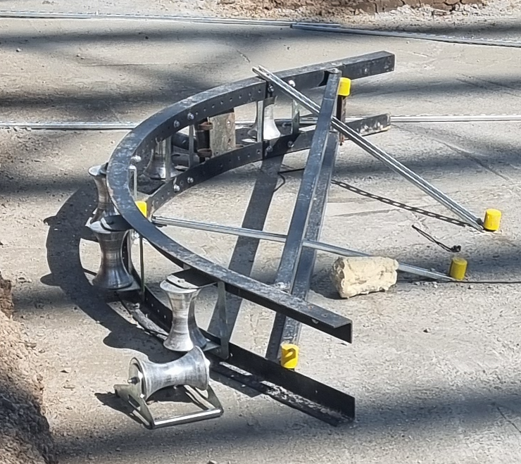 Construction equipment on a paved surface, including metal rails, supports, yellow caps, and a brick resting on the ground.