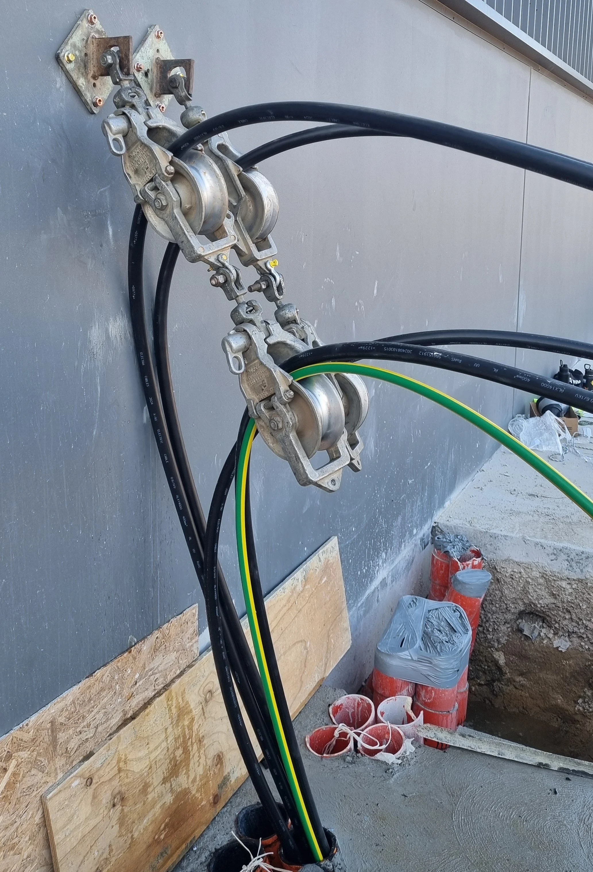 Electrical cable pulling through underground conduits using pulleys mounted on a concrete wall.