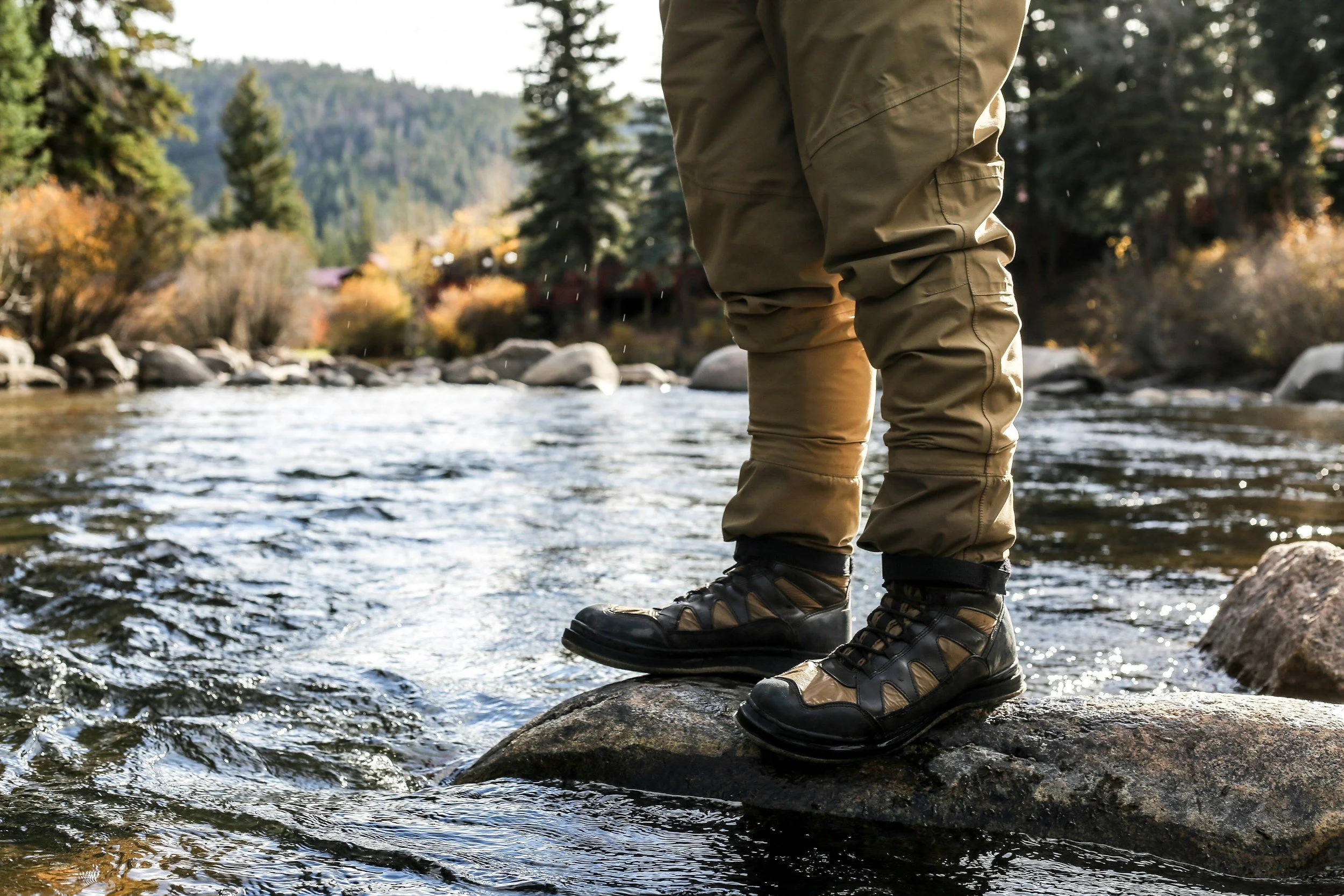 Person wearing hiking boots and khaki pants standing on a rock in a river.