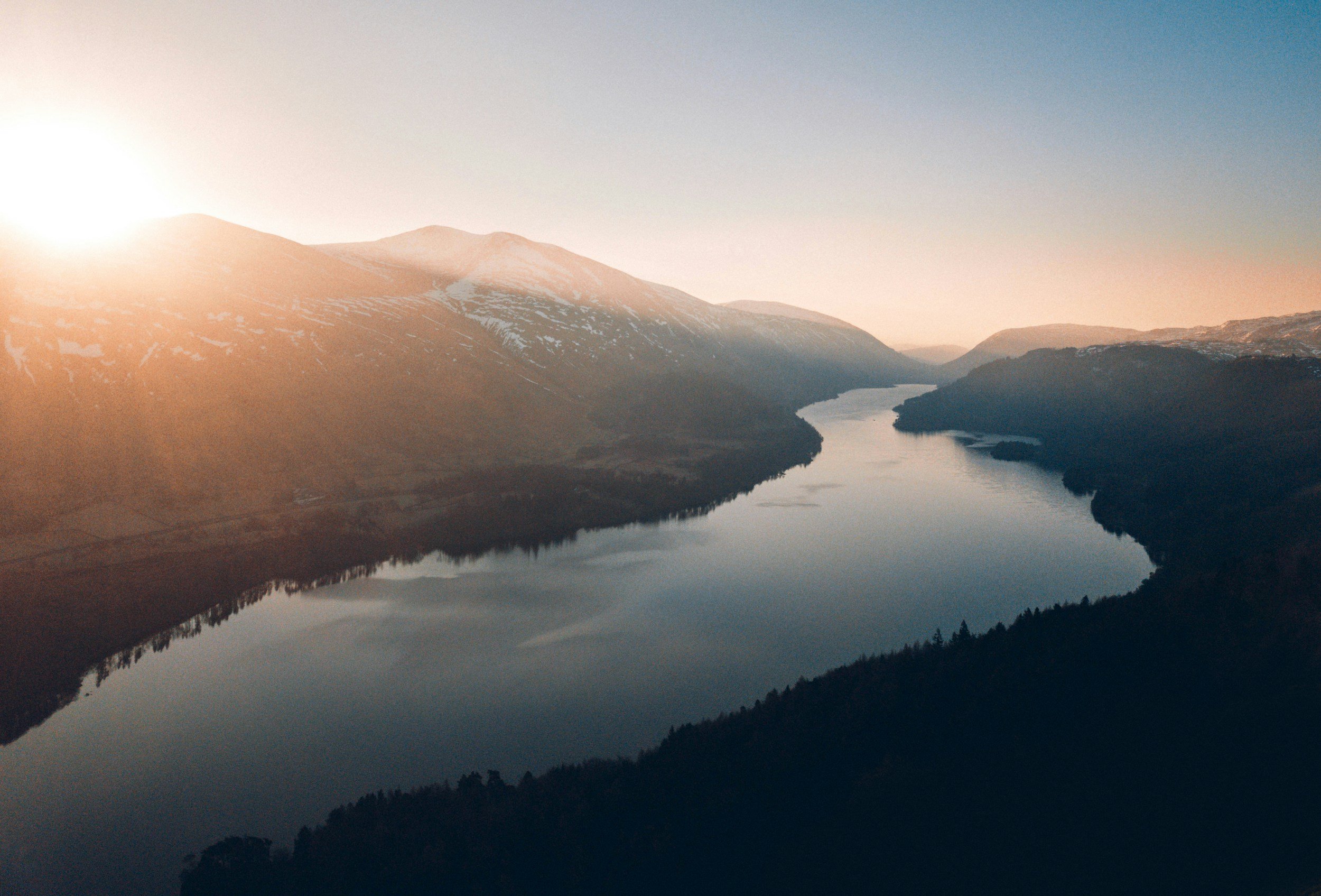 A scenic view of a river winding through a mountainous landscape during sunrise or sunset.