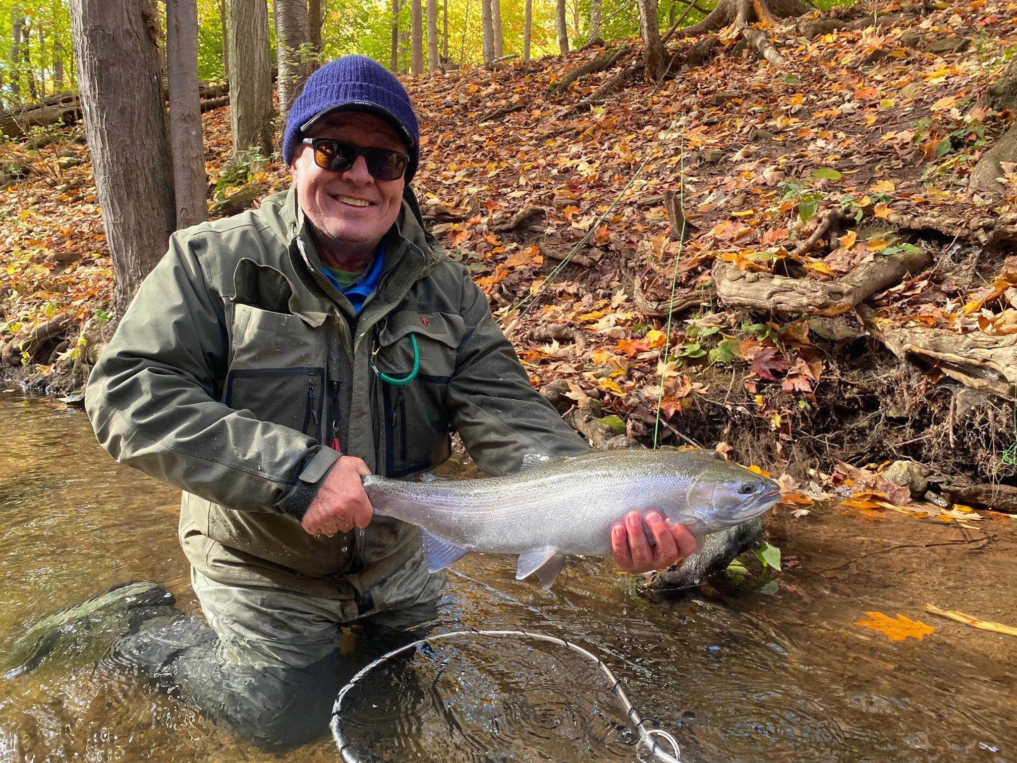 A man holding a fish in a river during fall.