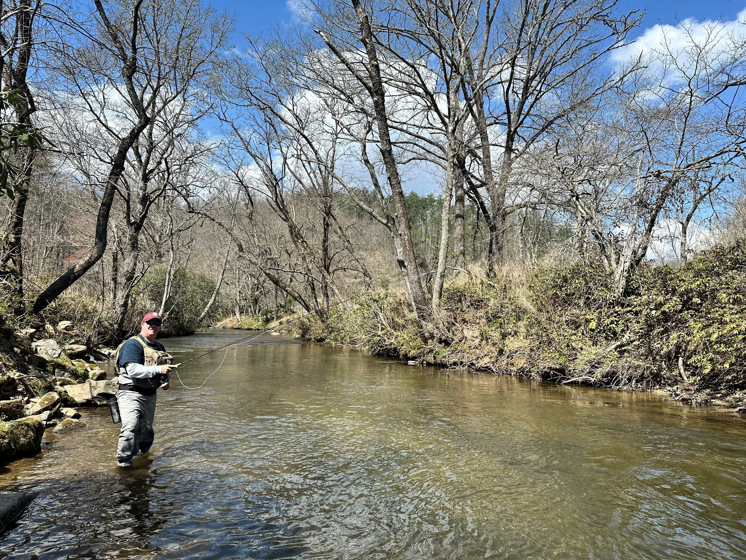 Man fishing in a creek surrounded by leafless trees