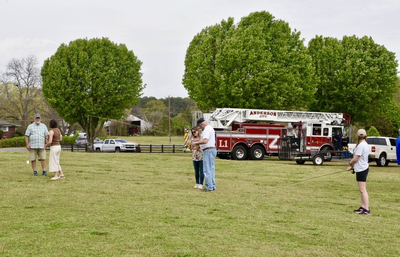 People at a park during daytime, with a fire truck and trees in the background.