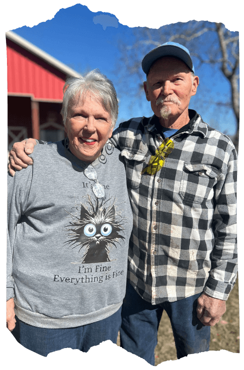 Liz and Julius Stuart standing outside on their family ranch in Richmond, Texas. Behind them is a red barn and a clear blue sky.