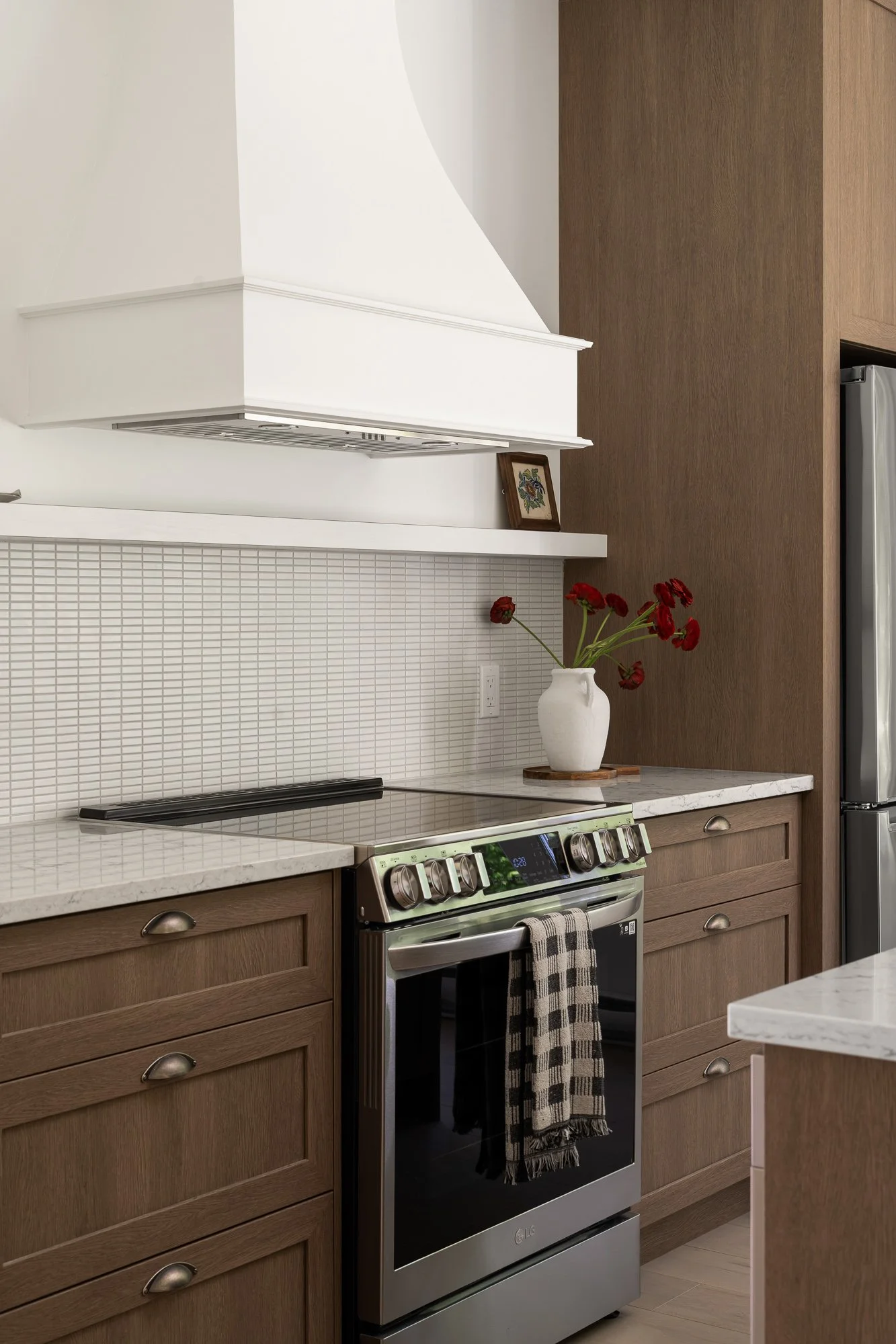 Aménagement de cuisine par Studio Lagom au Lac-Brome, combinant des armoires en bois chaleureux, un dosseret en fine mosaïque et une grande hotte blanche sur mesure.