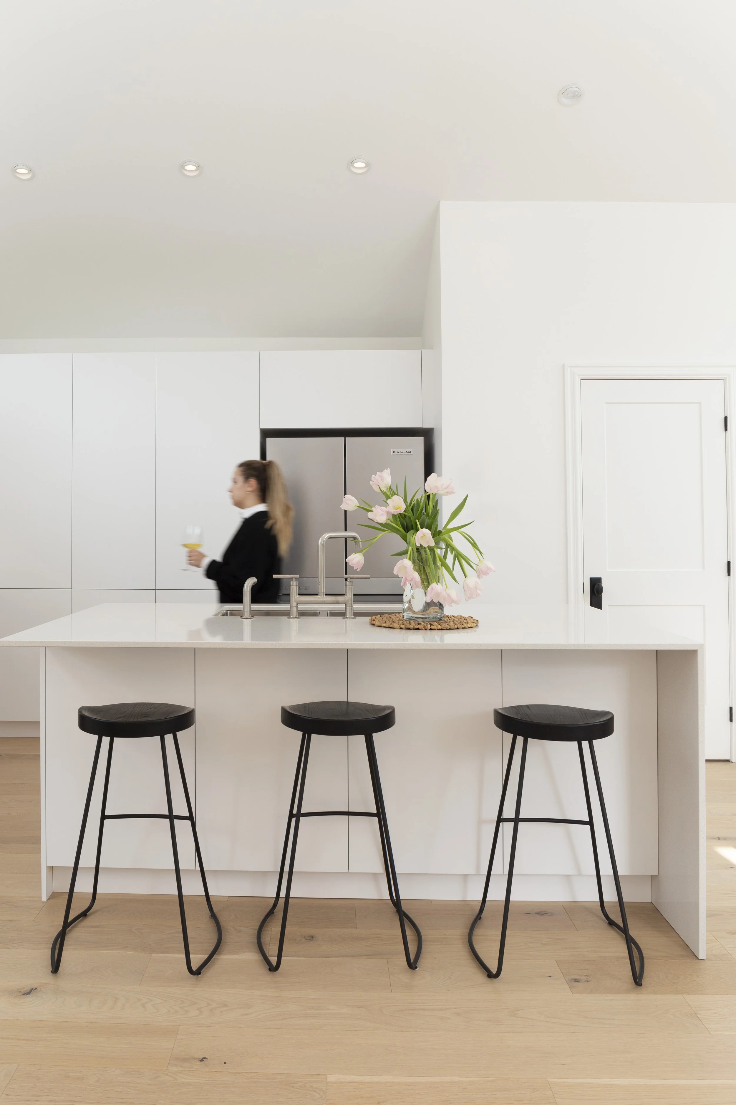 Design d'intérieur d'une cuisine minimaliste blanche avec îlot central et tabourets de style industriel, une réalisation de Studio Lagom.