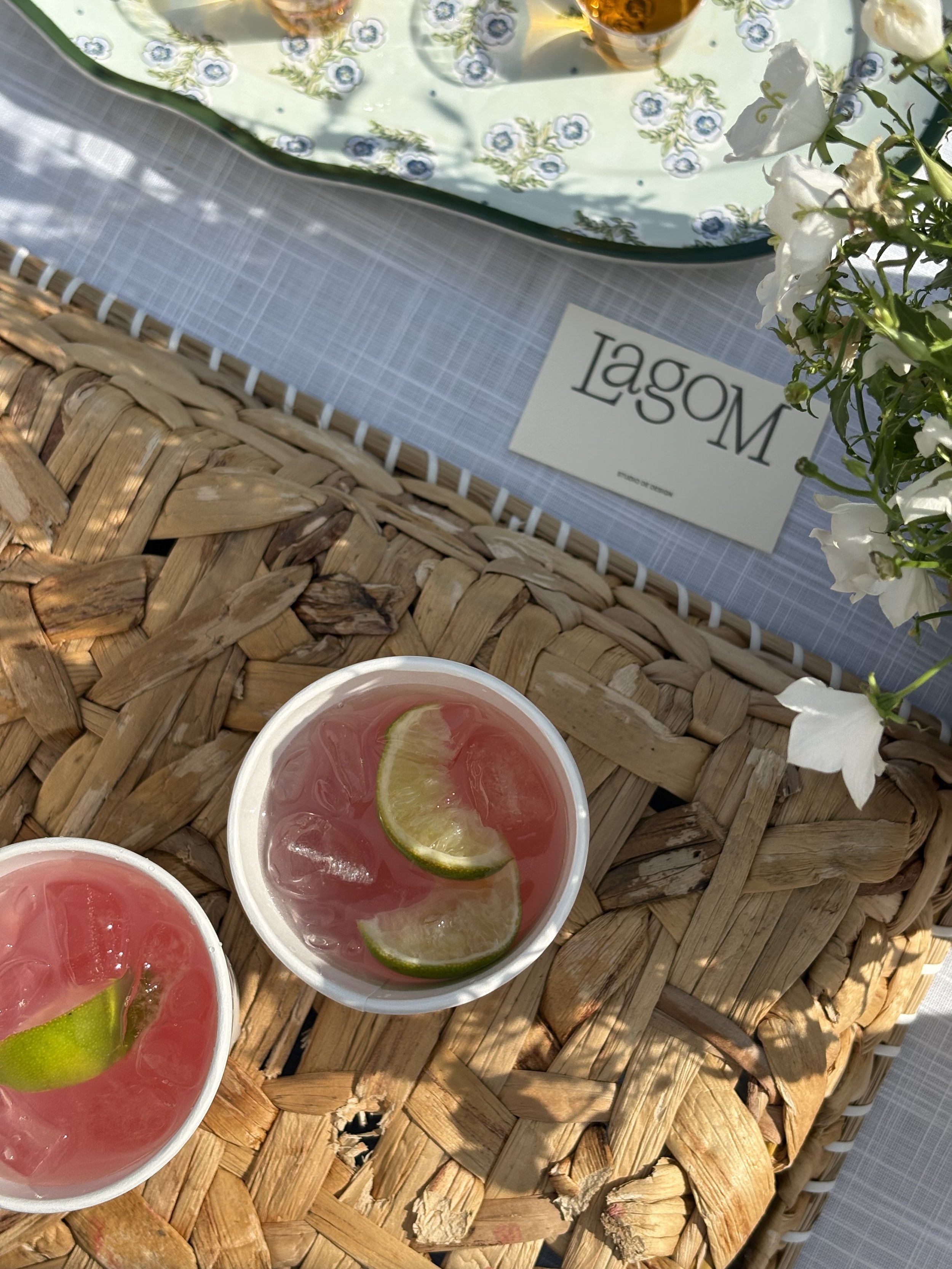 Mise en scène estivale par Studio Lagom, illustrant une carte d'affaires du studio de design à côté de boissons fraîches sur un plateau en fibres naturelles.