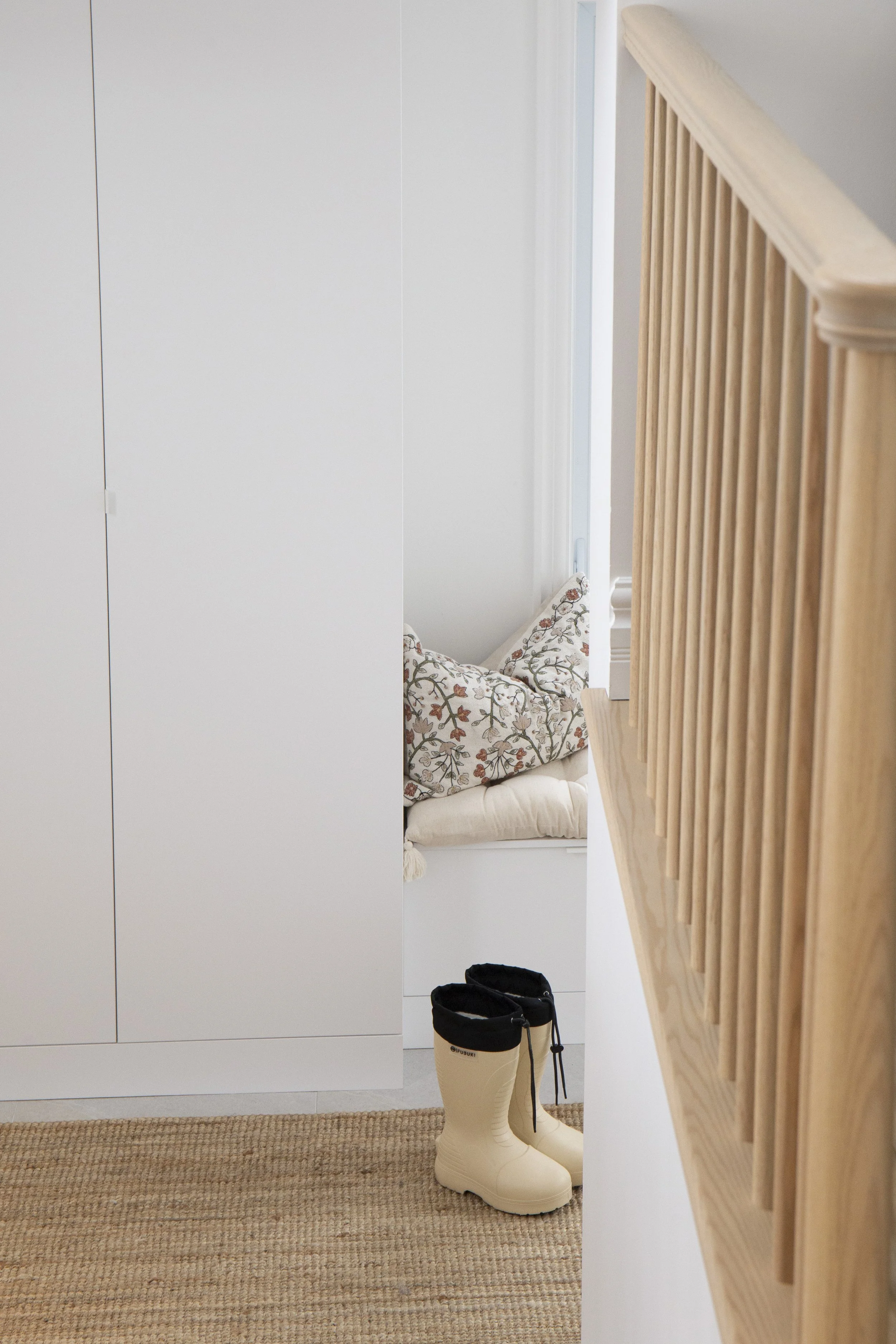Design d'intérieur d'une entrée lumineuse avec rangement sur mesure blanc et rampe en bois naturel, une réalisation de Studio Lagom.