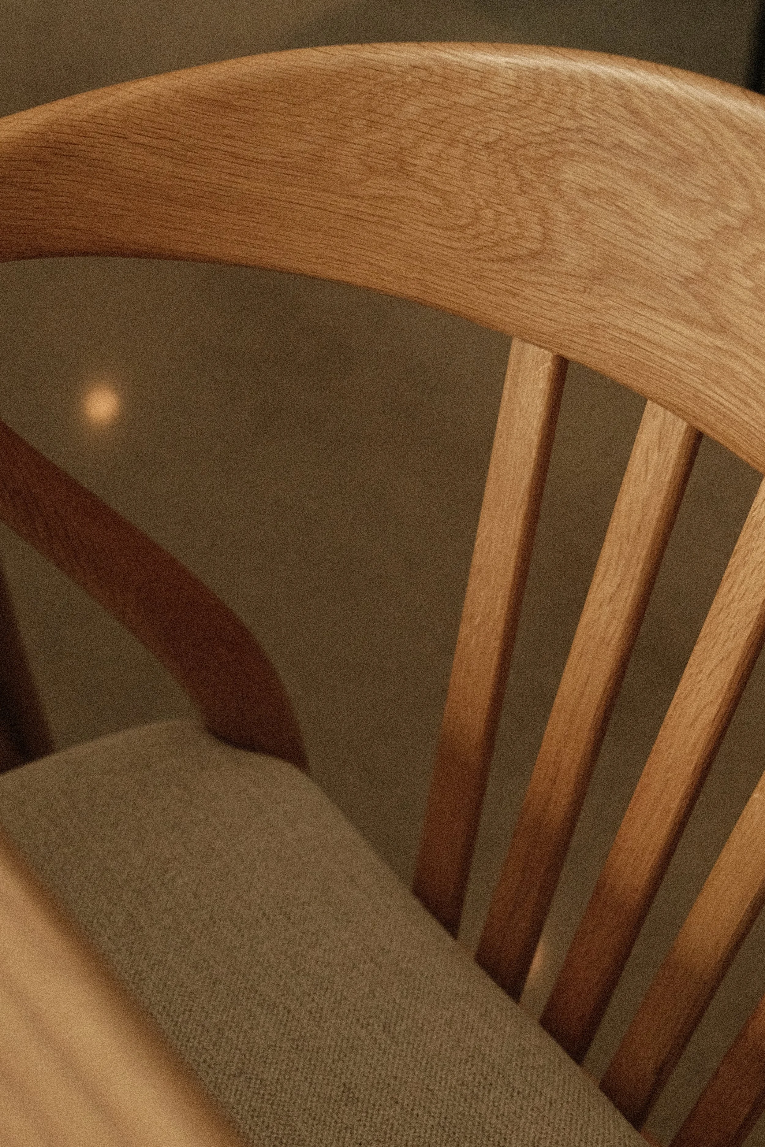 Détail de menuiserie sur une chaise scandinave en bois massif (chêne clair) par Studio Lagom, montrant le dossier incurvé à barreaux et l'assise rembourrée en tissu texturé beige.