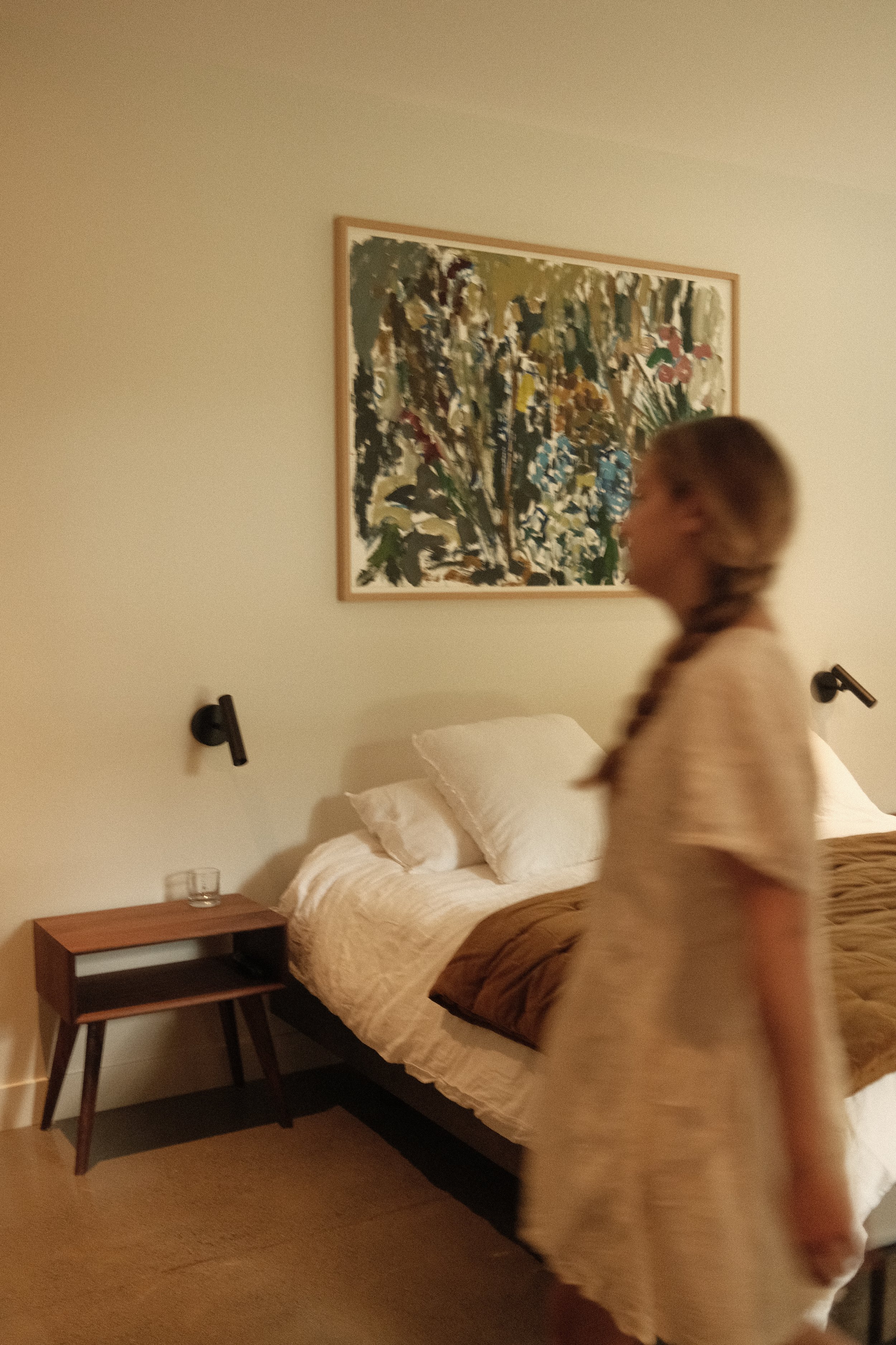 Chambre à coucher chaleureuse conçue par Studio Lagom avec mobilier en bois, appliques murales noires et œuvre d’art abstraite.